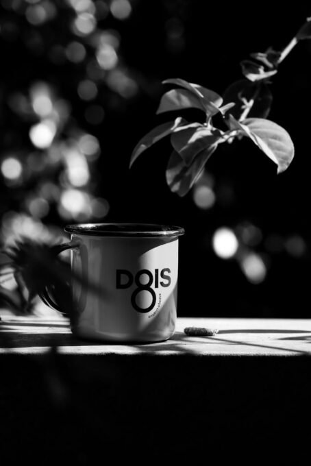 Black and white photo of a metal mug on a table with leaf shadows.