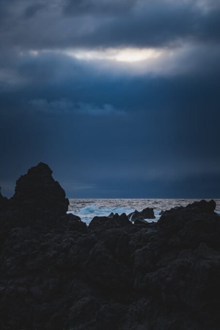 Dark rocky seashore under moody clouds at dusk in Portugal, capturing dramatic scenery.