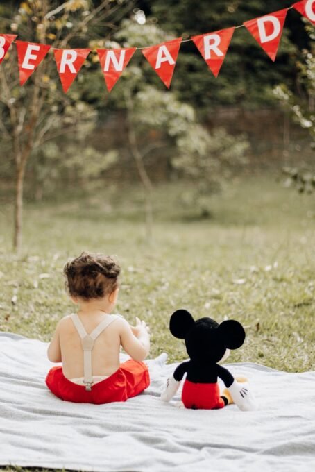 A baby sits with a toy on a blanket under a birthday banner in São Paulo park.