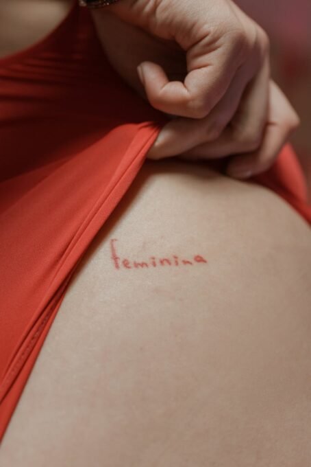 A close-up image showing a red 'feminina' tattoo partially covered by red fabric.